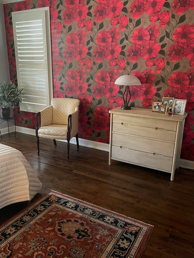 Bedroom wall featuring wallpaper printed with Bees & Poppies design in red.