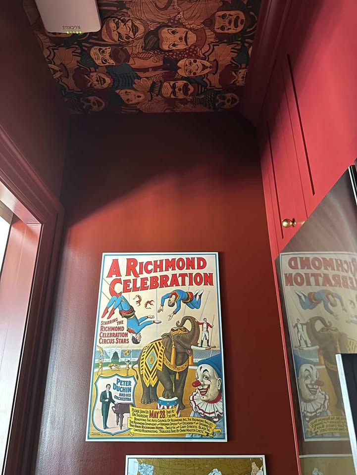 Vintage poster, "A Richmond Celebration" featuring big top performers, framed on the wall of the red pantry, with a view of the wallpapered ceiling above.