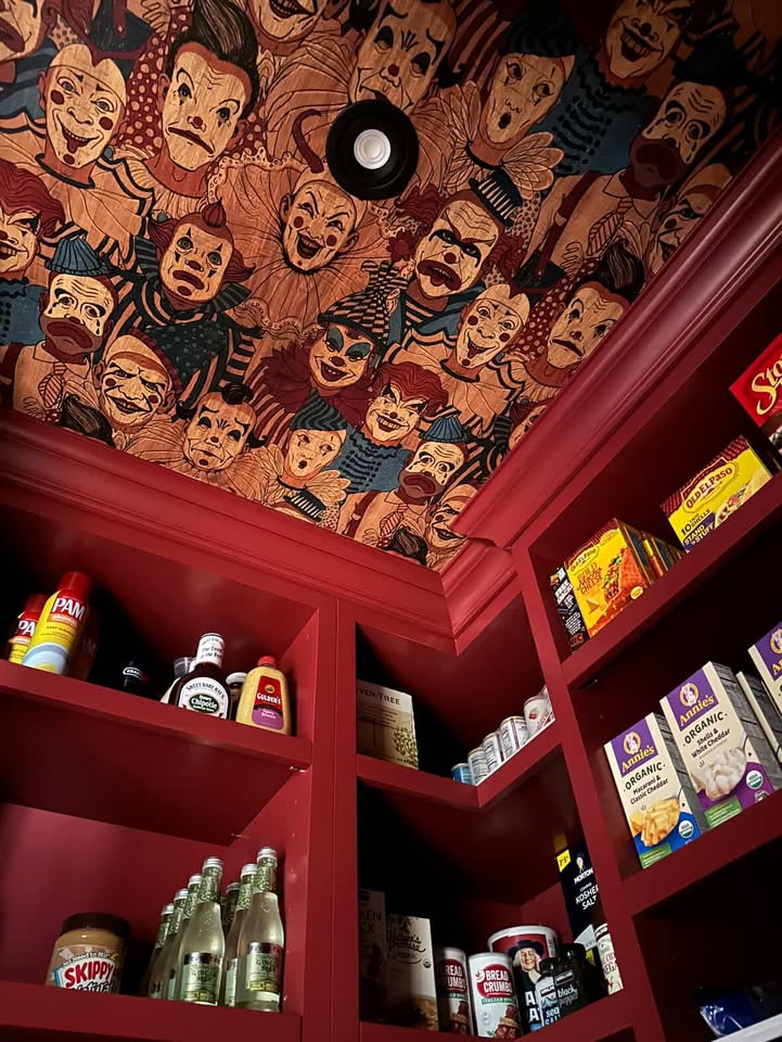 Looking up to the ceiling to see the tops of the dark red pantry shelves filled with food, the ceiling is wallpapered with the creepy clowns.