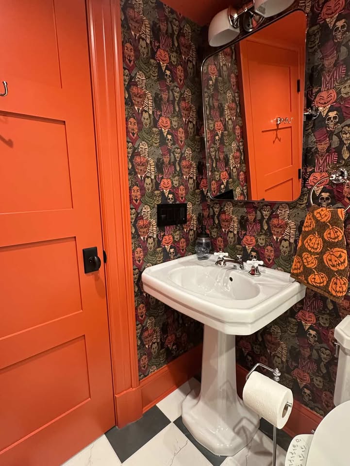 Orange door and woodwork frame the walls papered with creepy halloween creatures in this black and white bathroom.