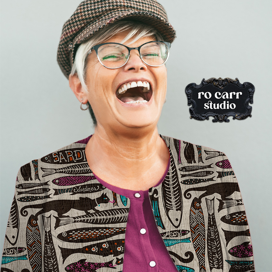 Middle aged woman with a big smile and a flat cap, wearing a collarless jacket printed with the pattern.