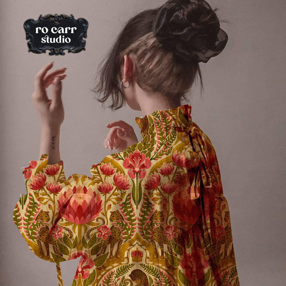 A woman wearing a loose ruffled blouse printed with a damask leopard and floral pattern in gold, green, and rose.