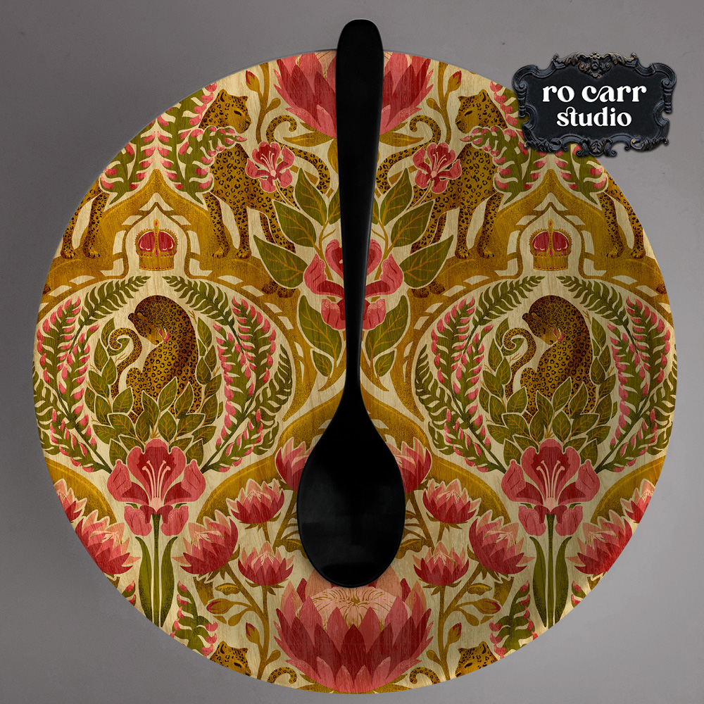A circular fabric swatch of a damask leopard and floral pattern in antique gold, olive, and rose, shown with a black wooden spoon.