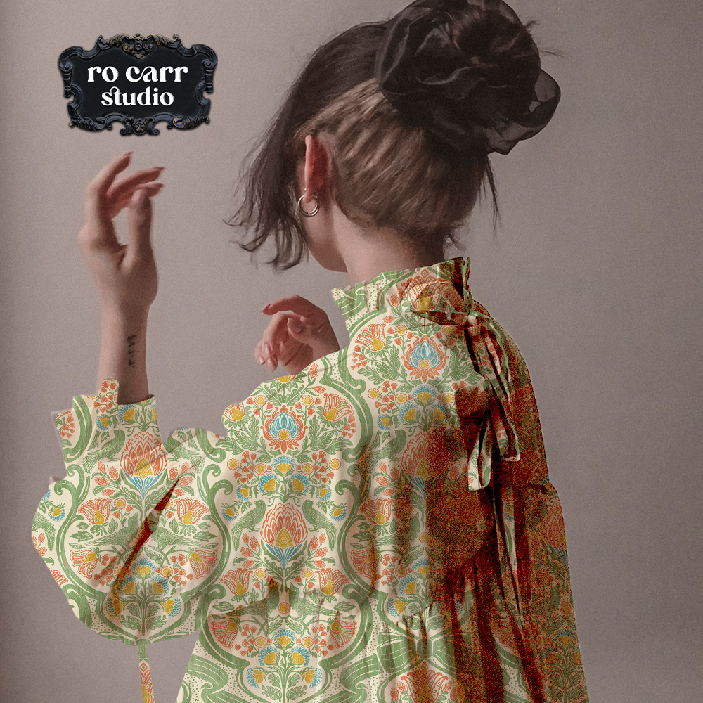 Woman wearing a loose ruffled blouse in a botanical chintz print with coral, teal, and gold on green.