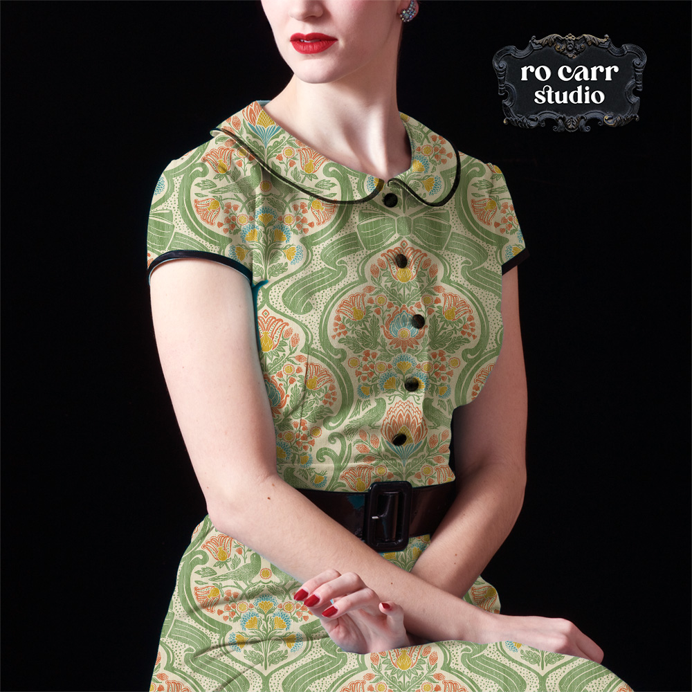 Model in a fitted Peter Pan collar dress in botanical chintz print, seated against a dark background.