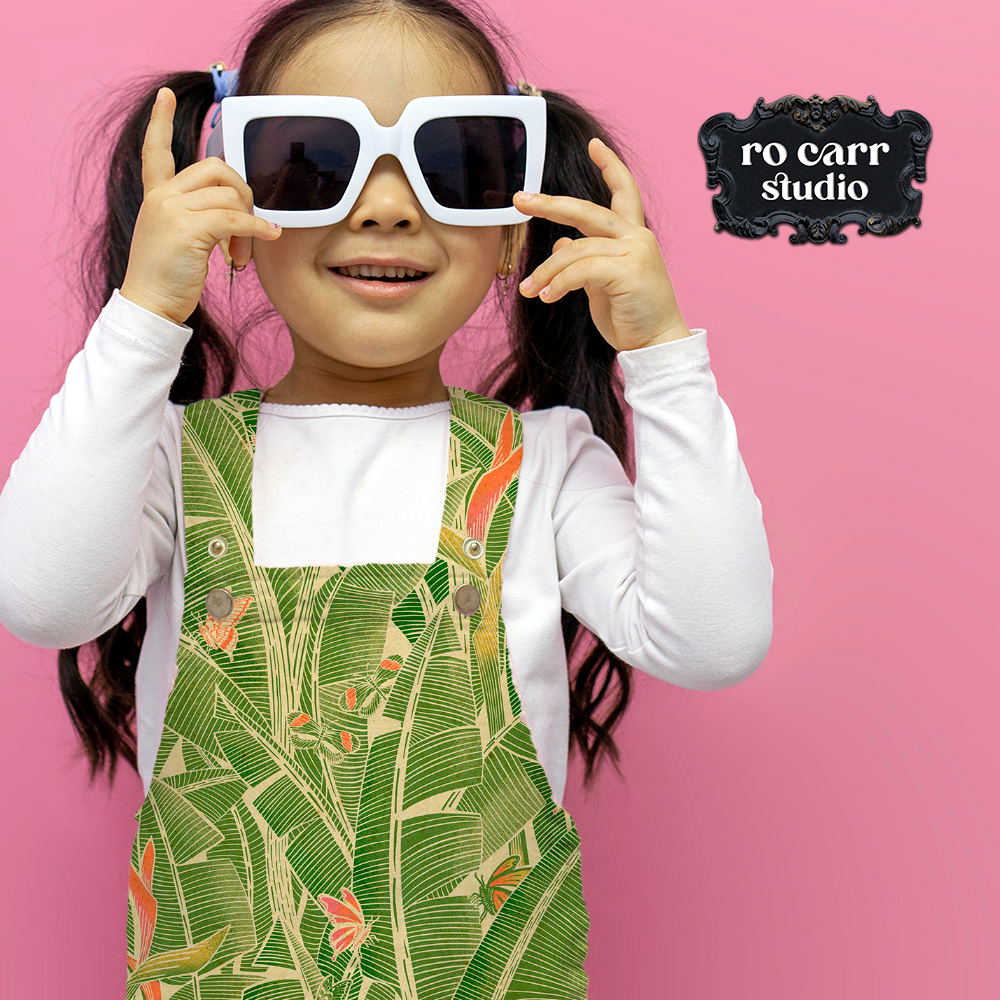 Young girl in a Goodnight Jungle pinafore dress holding oversized white sunglasses.